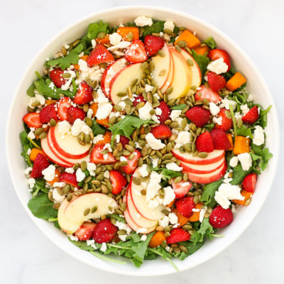 green salad with apple slices, pepitas, crumbled white cheese, and strawberries