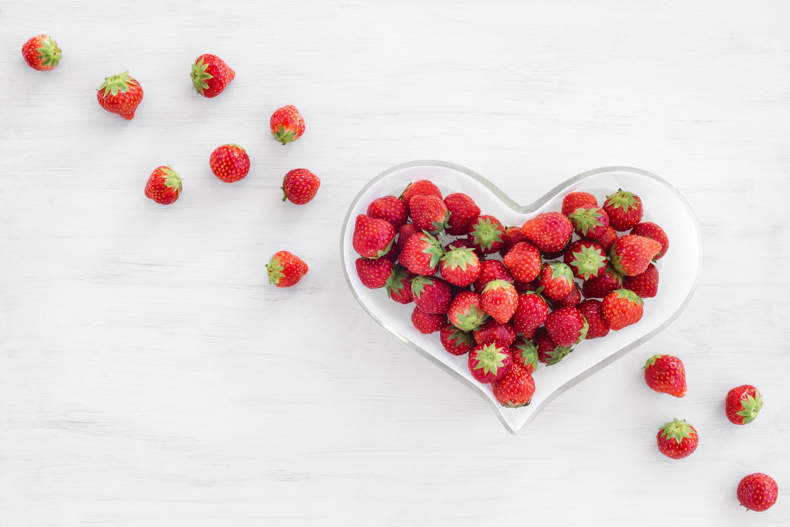 Strawberries in a heart-shaped bowl, on white wooden background.